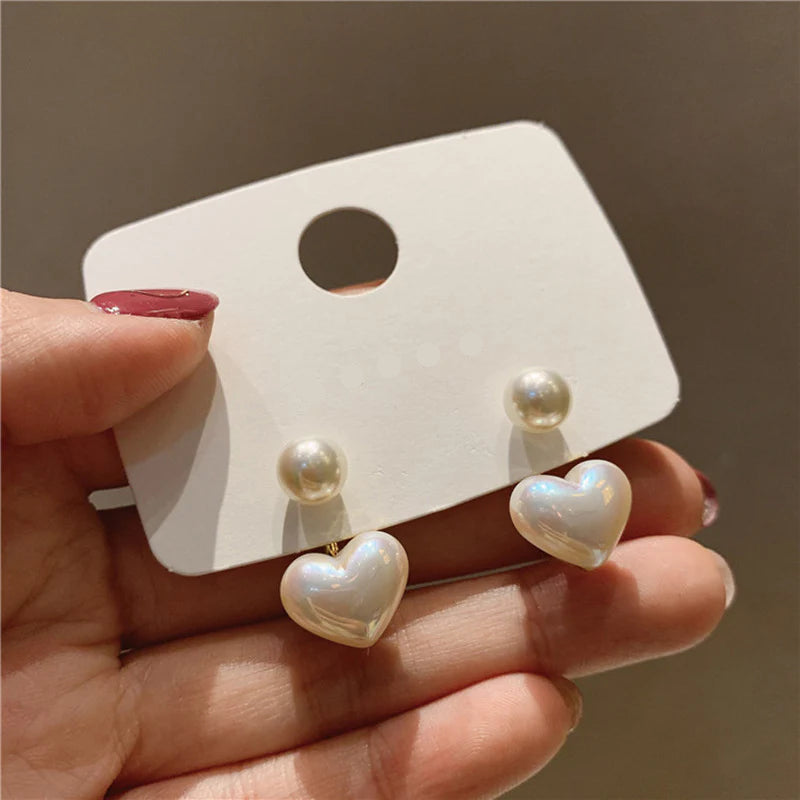 Heart-shaped pearl earrings on a REINA branded card held by a hand.